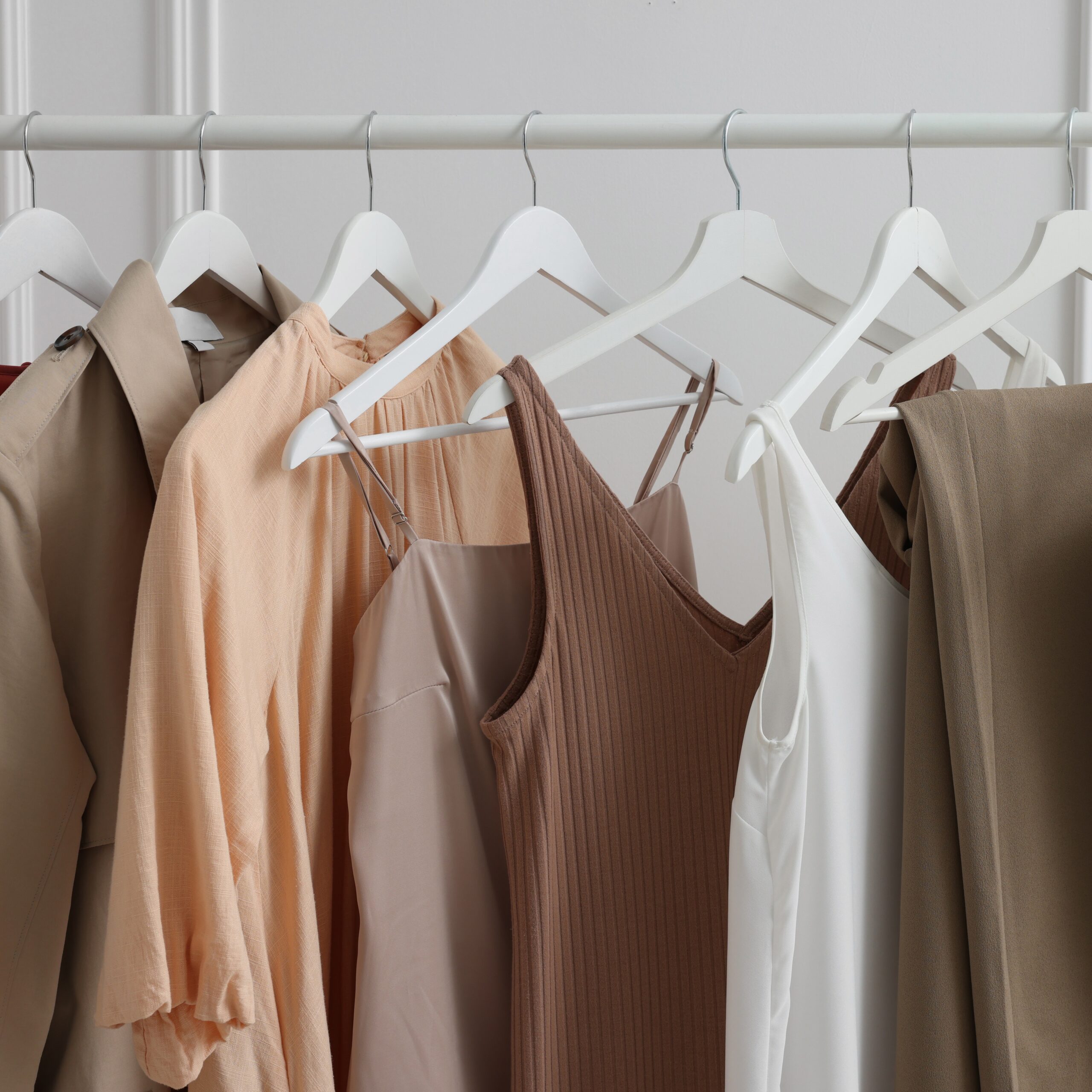 Rack with different stylish women`s clothes near white wall indoors, closeup